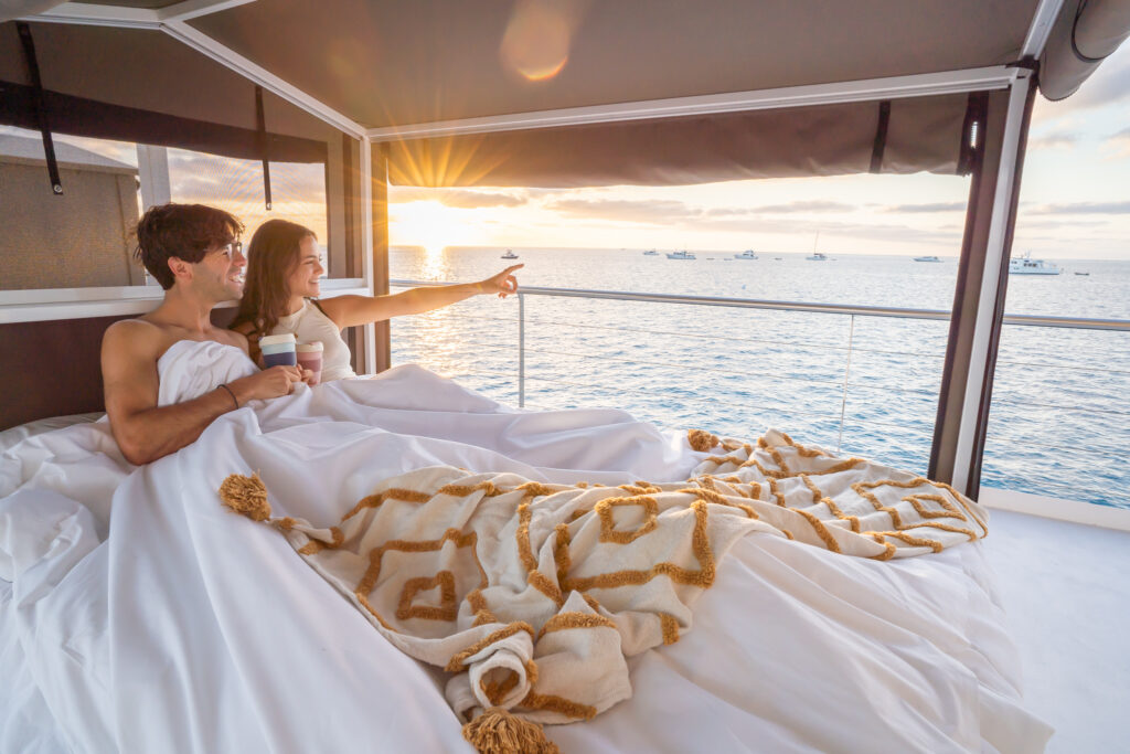 Couple watching the sunrise from a glamping bed on Lady Musgrave HQ, moored on the reef